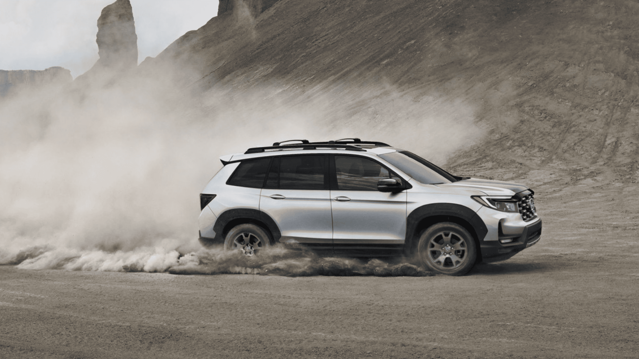 Silver Honda Passport SUV kicking up dust while off-roading in a rugged desert landscape.
