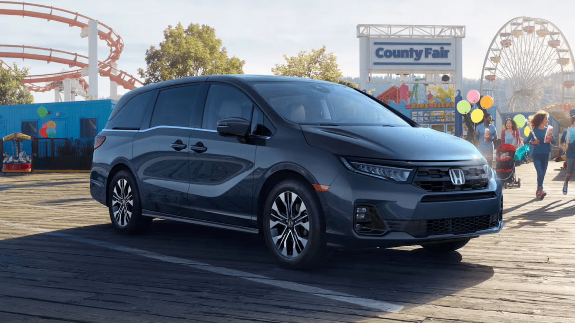Silver 2025 Honda Odyssey parked in front of a colorful playground on a cloudy day.
