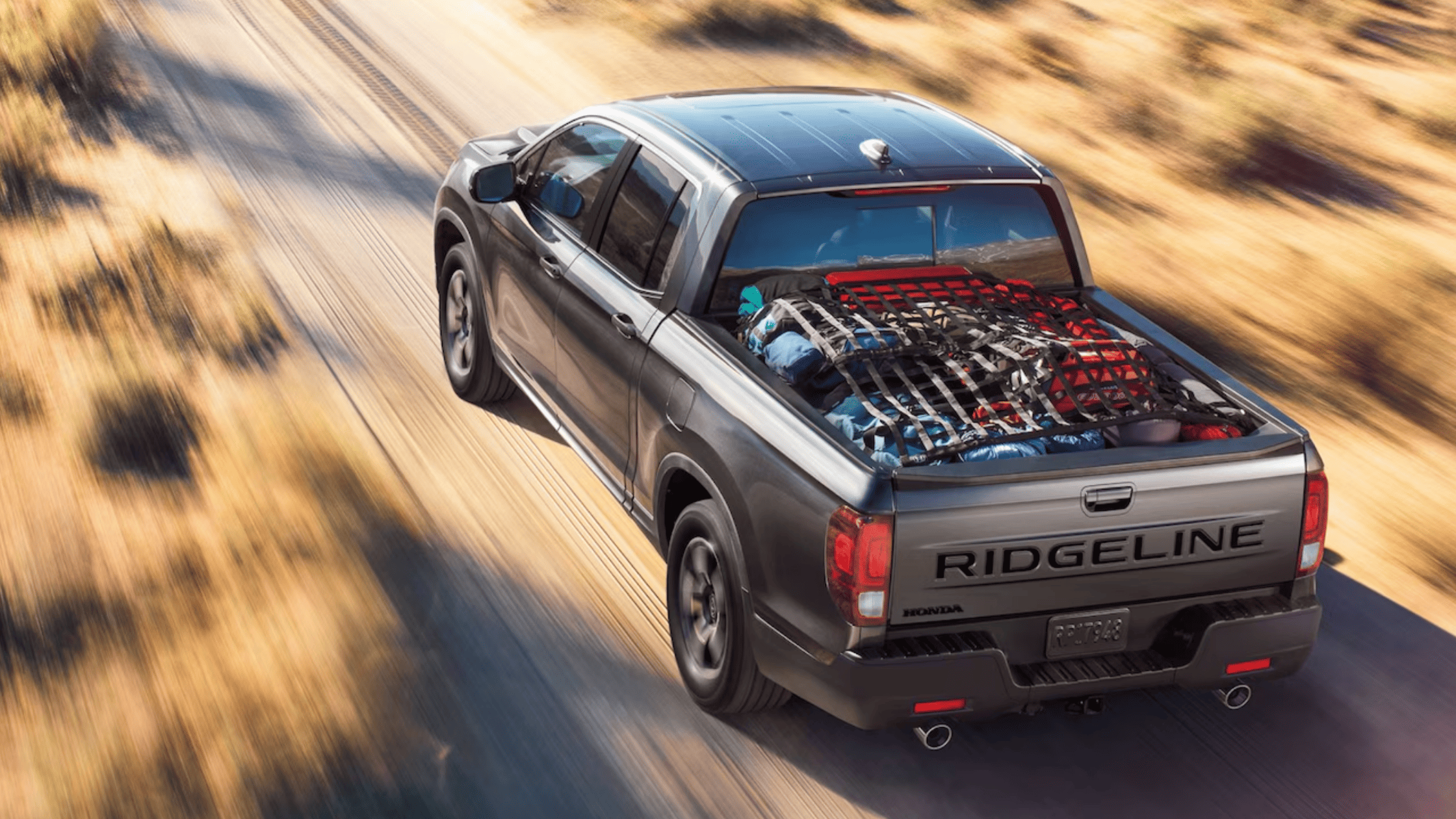 Rear view of a Honda Ridgeline truck kicking up dust on a rugged trail.